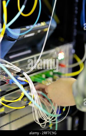 le mani del tecnico inseriscono i cavi in fibra ottica nello switch montato su rack Foto Stock