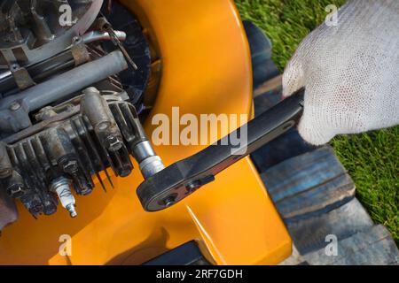 Un primo piano dettagliato di un uomo che ripara sapientemente un rasaerba, mostrando la complessità della manutenzione delle attrezzature per il taglio del prato. Foto Stock