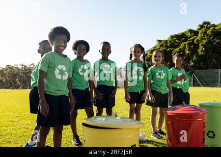 Ritratto di bambini felici e diversi che raccolgono riciclano sorridendo nel soleggiato campo della scuola elementare Foto Stock