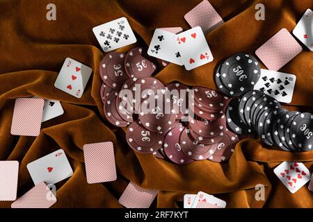 Le fiche da poker rosse e nere sono sparse sul tessuto marrone, mentre le piccole carte da gioco sono sparse. Foto Stock