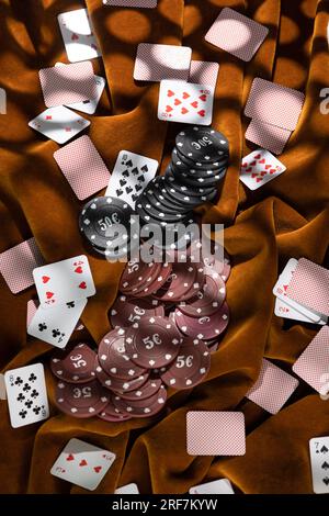 Le fiche da poker rosse e nere sono sparse sul tessuto marrone, mentre le piccole carte da gioco sono sparse. Foto Stock