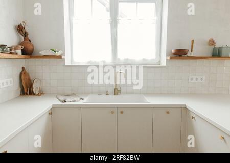 Eleganti armadi da cucina bianchi, rubinetto in ottone e lavandino in granito, ripiani in legno con utensili nella nuova casa scandinava. Cucina dal design moderno e minimalista. Foto Stock
