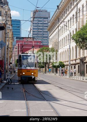 Il tram giallo, noto anche come tram, si trova in una strada nella città di Sofia, in Bulgaria. Blocco di appartamenti dietro. 1° agosto 2023. Foto Stock