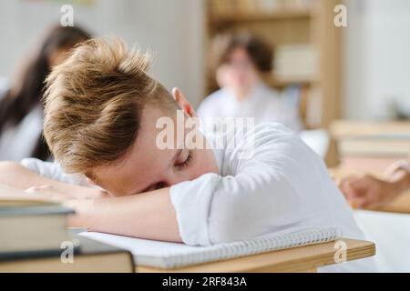 Scolaro stanco che dorme alla scrivania durante la lezione in classe Foto Stock