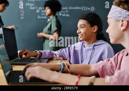 Gli studenti che lavorano online con il software sul laptop mentre sono seduti insieme a un tavolo in classe Foto Stock
