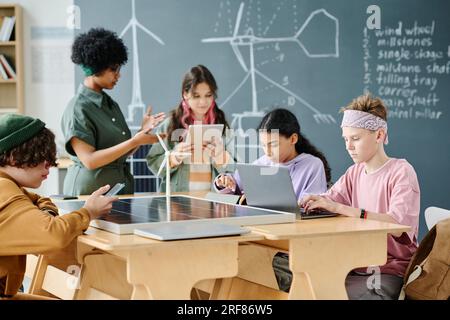 Gruppo di studenti che utilizzano gadget per apprendere nuove tecnologie con l'insegnante durante la lezione in aula Foto Stock