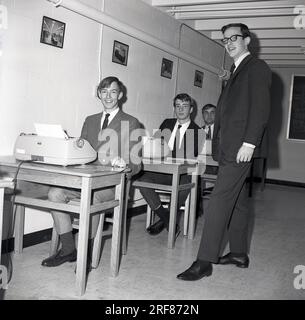 Anni '1960, studenti maschi storici e ben vestiti del college d'affari seduti alle piccole scrivanie di una classe che utilizzava macchine da scrivere elettriche, supervisionati da un giovane insegnante adulto in una classe di digitazione, Middletown, USA. Il modello di macchina da scrivere utilizzato è la macchina da scrivere IBM Selectric, introdotta per la prima volta sul mercato nel 1961. Foto Stock