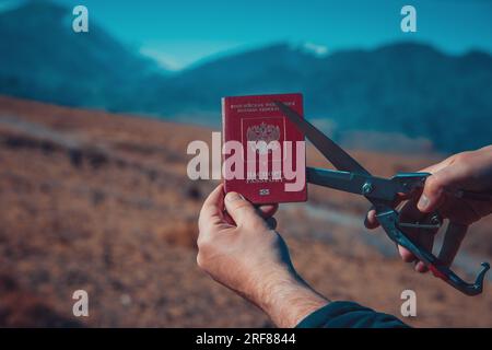 Uomo che taglia il passaporto russo sulle montagne, concetto di immigrazione Foto Stock