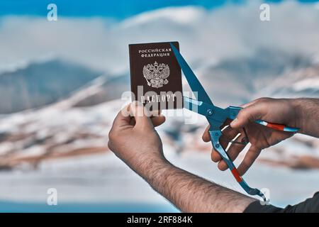 Uomo che taglia il passaporto russo sulle montagne, concetto di immigrazione Foto Stock