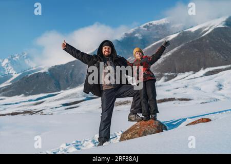 Buon padre e bambino che salutano le mani e si stendono sullo sfondo delle montagne durante la stagione invernale Foto Stock