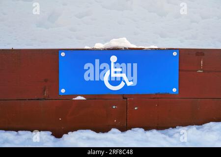 Cartello parcheggio per disabili su una recinzione di legno bassa in inverno, primo piano. Foto Stock