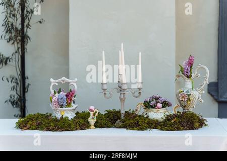 Decorazione decorativa del tavolo festivo. Candelabro con candele, vasi con giacinti e altri fiori, muschio verde su un tavolo coperto da un Foto Stock