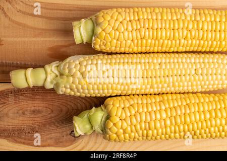 Tre pannocchie di mais biologico dolce, primo piano, su un tavolo di legno, vista dall'alto. Foto Stock