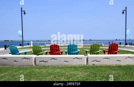 Fila di sedie vuote colorate per prato Adirondack lungo la parete del porto Foto Stock