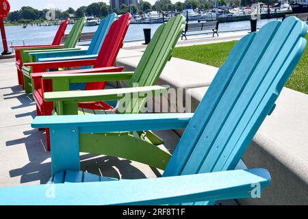 Fila di sedie vuote colorate per prato Adirondack lungo la parete del porto Foto Stock