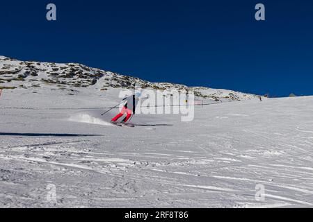 Falcade, Italia - 15 febbraio 2023: Pista da sci con sciatore sotto il cielo azzurro. Le persone guidano lungo le montagne innevate con gli sci. Gruppo di sciatori su una pista da sci Foto Stock