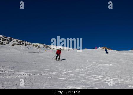 Falcade, Italia - 15 febbraio 2023: Pista da sci con sciatore sotto il cielo azzurro. Le persone guidano lungo le montagne innevate con gli sci. Gruppo di sciatori su una pista da sci Foto Stock