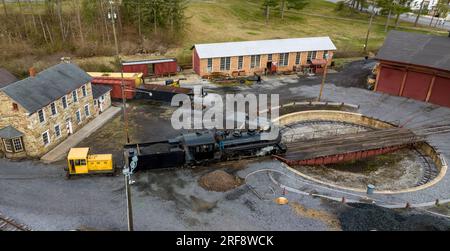 Vista droni di una locomotiva a vapore a scartamento ridotto che scende da un giradischi e si prepara per le giornate di lavoro in una giornata di sole primaverili Foto Stock