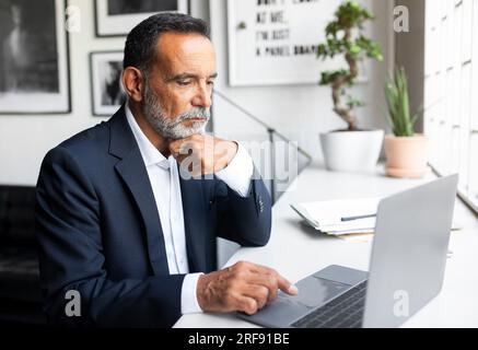 Calma fiducioso serio concentrato uomo d'affari senior caucasico nella digitazione di tute al computer Foto Stock