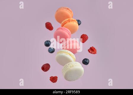 Macaron e bacche dolci volanti su sfondo lilla Foto Stock