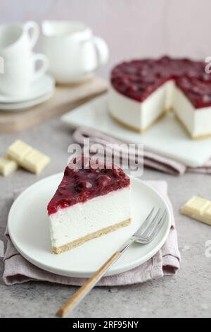 Cioccolato bianco senza cottura e cheesecake di ciliegia su un piatto bianco. Tazze di caffè bianche e sfondo rosa. Foto Stock