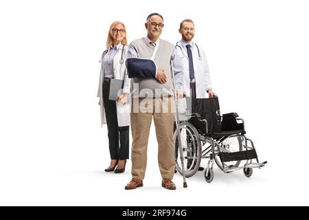 Uomo maturo con stampelle e imbracatura per braccio in piedi di fronte a un medico con una sedia a rotelle isolata su sfondo bianco Foto Stock