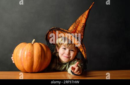 Simpatico ragazzo con cappello da strega con jack-o-lantern di Halloween. Bambino sorridente in cappello da strega con zucca di Halloween. Trick o dolcetto. Preparazione per Halloween Foto Stock