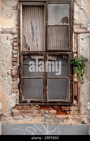 Esterno di un vecchio edificio abbandonato con muri in pietra sgretolanti e piccole finestre situate sulla strada di una piccola città Foto Stock