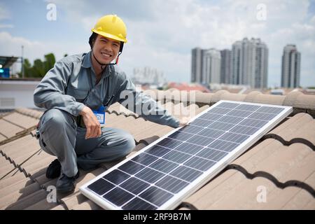 Appaltatore asiatico positivo che installa pannelli solari sul tetto di piastrelle Foto Stock