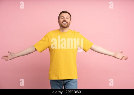 Ritratto di un giovane felice che spalanca le braccia per abbracciarti con gli occhi chiusi isolati sul rosa Foto Stock
