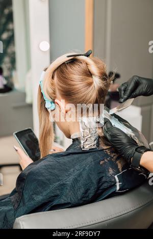 Bionda morente in un salone di bellezza. Le mani del parrucchiere con i capelli del cliente Foto Stock