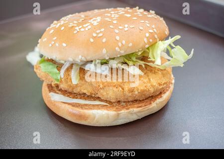 Hamburger di pollo condito con lattuga fresca, servito sullo sfondo di un'ombra naturale nera. Una delizia visiva e una messa a fuoco selezionata. Foto Stock