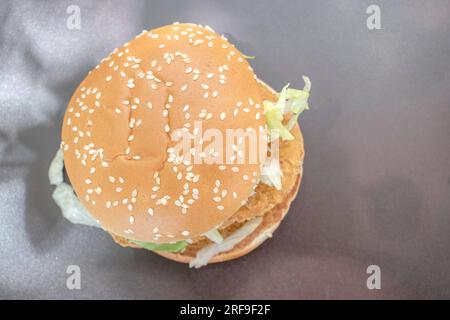 Hamburger di pollo condito con lattuga fresca, servito sullo sfondo di un'ombra naturale nera. Una delizia visiva e una messa a fuoco selezionata. Foto Stock