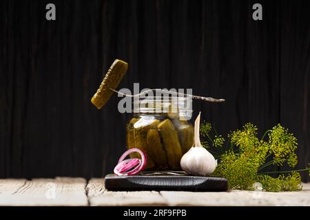 Cetrioli in scatola in un vaso aperto, un cetriolo su una forchetta vintage giace sulla parte superiore, sfondo scuro. Foto Stock