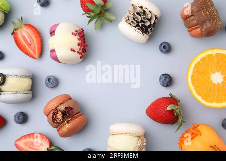Cornice composta da deliziosi macaron, arancia e frutti di bosco su un tavolo azzurro, piatto. Spazio per il testo Foto Stock