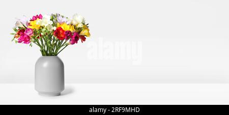 Vaso con bellissime freesie colorate su sfondo bianco e banner dal design Foto Stock