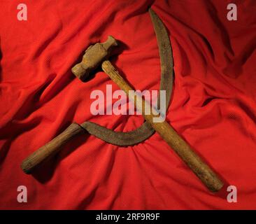 Antico martello e falce su tessuto rosso formano il simbolo dell'ex Unione Sovietica. Foto Stock