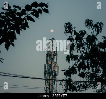 Cattura unica: Luna piena mattutina arroccata sulla cima di una torre di rete nella pittoresca Uttarakhand, India. Foto Stock