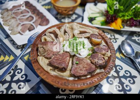 Piatto tradizionale asiatico kazako Beshbarmak: Tagliatelle con agnello e cipolle da vicino su un piatto sul tavolo. vicino al brodo in ciotole. dastarkhan. bolied Foto Stock