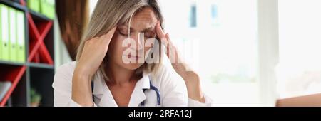 Medico di sesso femminile esausto che ha mal di testa durante il lavoro in clinica. Foto Stock