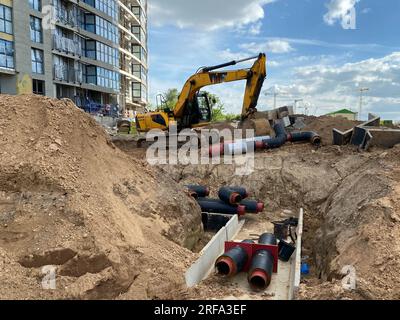 Potente escavatore industriale professionale giallo che esegue lavori di terra lavori di riparazione sotterranei e interramento di grandi tubi dell'acqua neri in un cantiere edile. Foto Stock