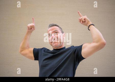 Attraente uomo atletico di mezza età che mostra le sue braccia muscolari puntando le dita verso l'alto Foto Stock