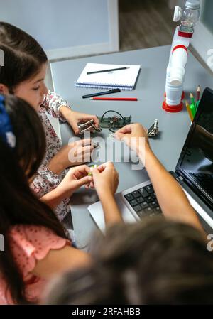 Insegnante donna irriconoscibile che aiuta le studentesse ad assemblare pezzi di macchina in una classe di robotica. Concetto elementare di educazione tecnologica. Foto Stock