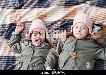 Due sorelle gemelle felici giacciono su una coperta in un parco autunnale. Le ragazze sorridono e guardano la telecamera, una delle sorelle si sta prendendo gioco e s Foto Stock