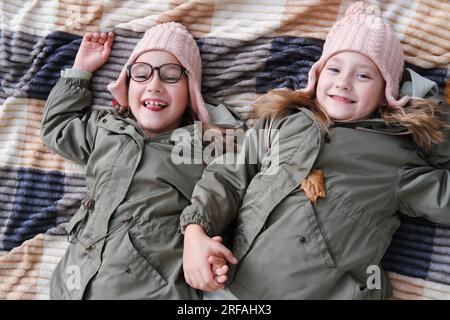Due sorelle gemelle felici giacciono su una coperta in un parco autunnale. Le ragazze sorridono e guardano la telecamera, una delle sorelle si sta prendendo gioco e s Foto Stock