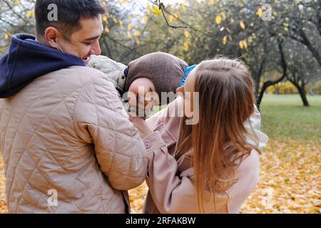 Genitori e figli trascorrono del tempo insieme nel parco autunnale. Padre che tiene un figlio in braccio, madre che solletico. Foto orizzontale Foto Stock