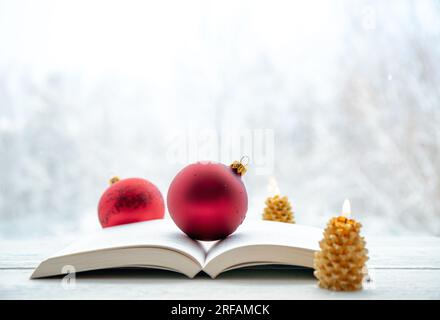 Libro di carta aperto con baule rosse tradizionali di Natale e candele in fiamme. Paesaggio invernale sfocato sullo sfondo. Molto spazio per le copie. Foto Stock