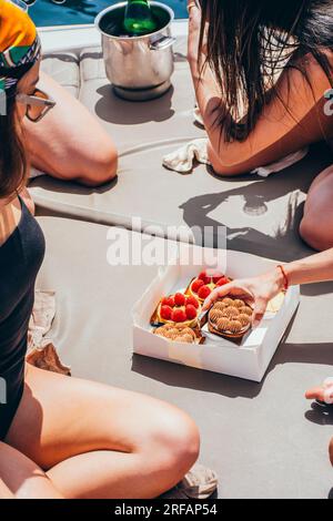 Gruppo di giovani donne con champagne e torte che si divertono su una barca che naviga sul mare in estate Foto Stock