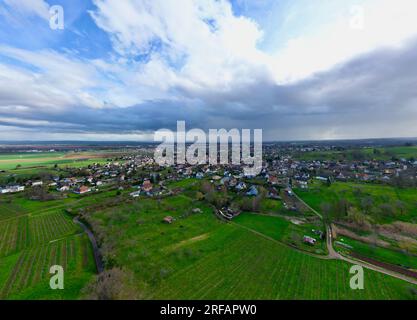 Uffholtz Winter Wonderland: I vigneti verdeggianti abbracciano un pittoresco villaggio tra cieli tempestosi, affacciati sulle pianure verdi alsaziane e sulle montagne Foto Stock