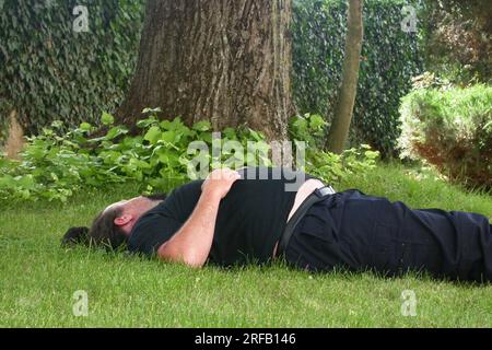 Un anziano senzatetto che dorme sdraiato nel parco Foto Stock